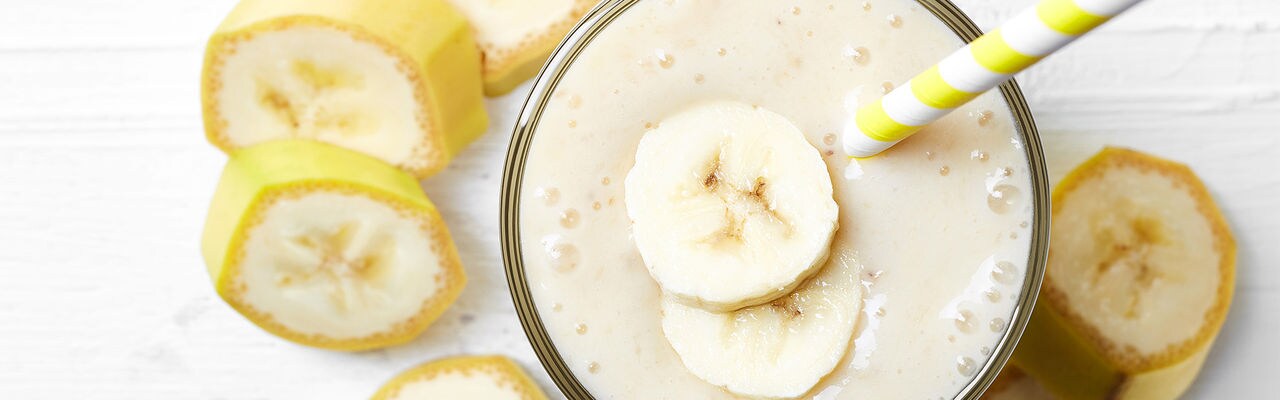Glass of banana smoothie on white wooden background from top view
