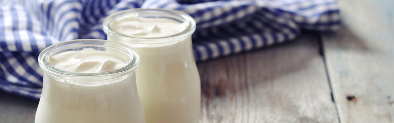 Greek yogurt in a glass jars with spoons on wooden background