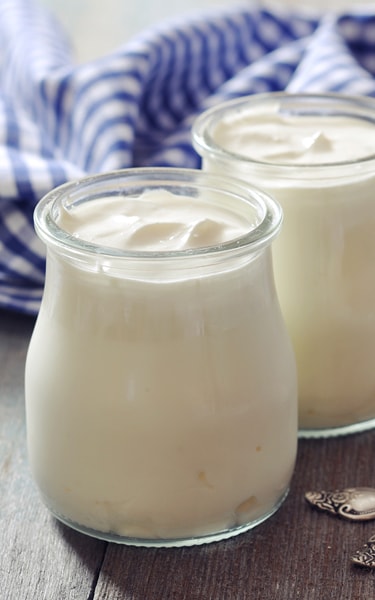 Greek yogurt in a glass jars with spoons on wooden background