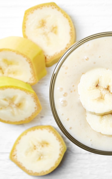 Glass of banana smoothie on white wooden background from top view