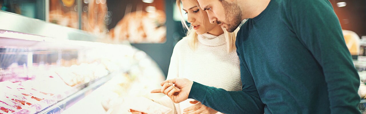 Closeup side view of a late 20's couple choosing some fresh meat for tonight's dinner. They are reading label on one of the packages and seem a bit uncertain about it.